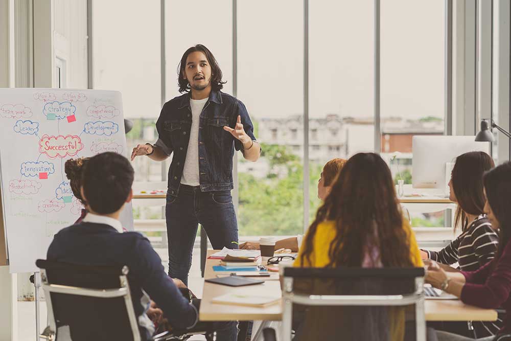 Young male student hosting a class workshop and speaking to his classmates