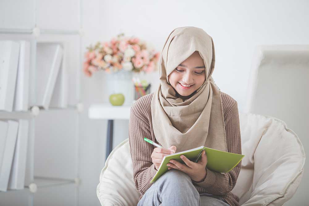 Young female student studying at home using a notepad and pen